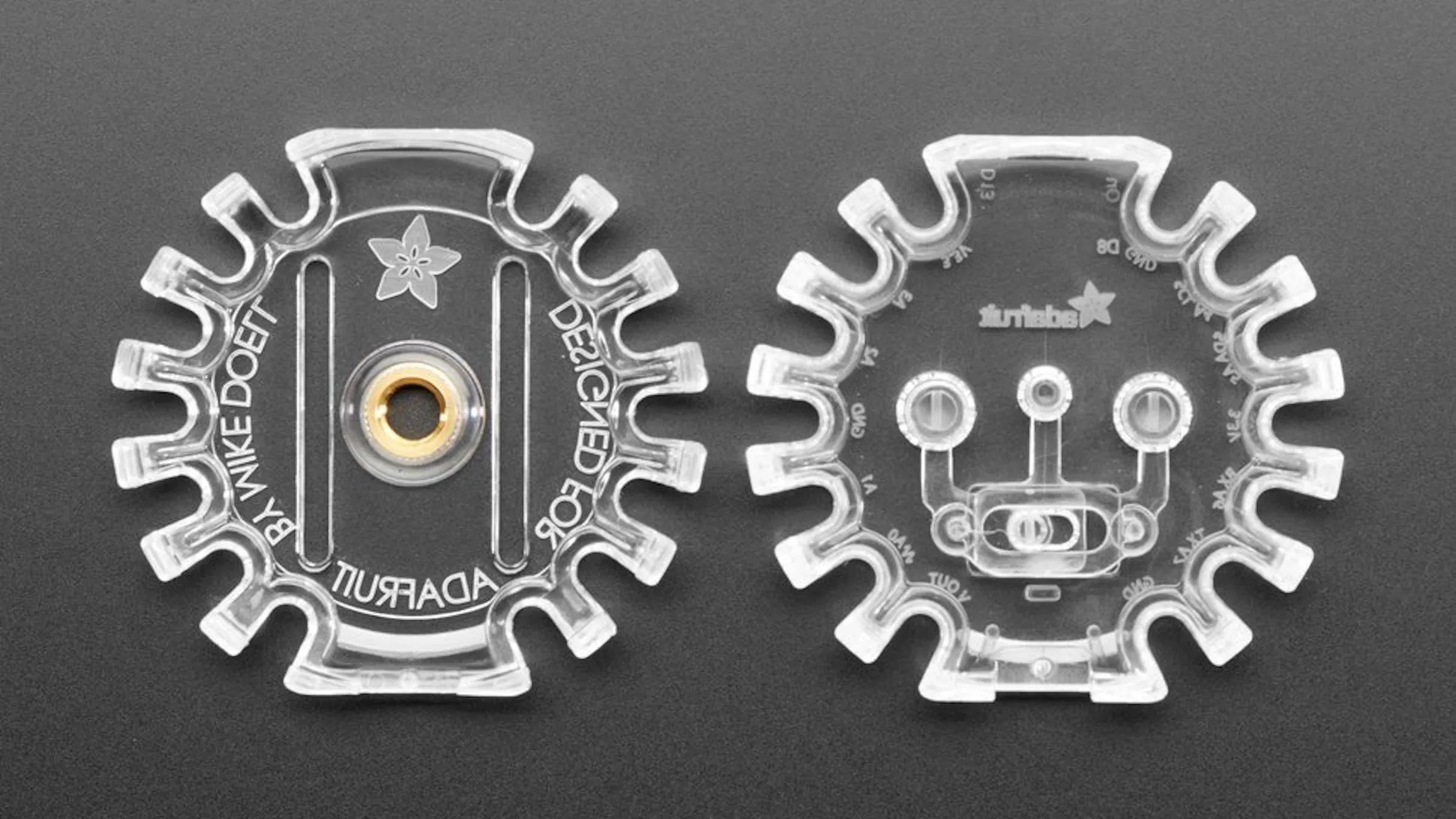 The two halves of the clear enclosure side by side, one embossed "Designed for Adafruit by Mike Doell"