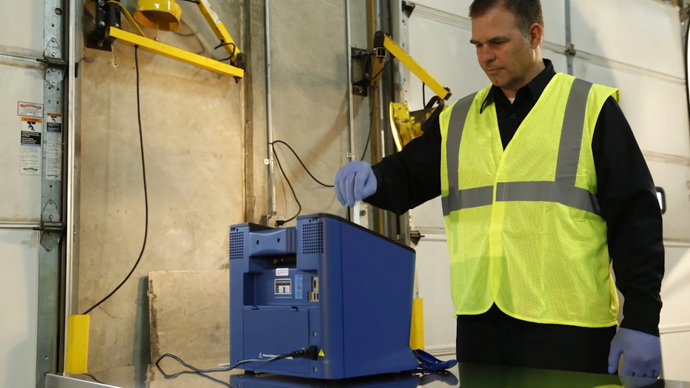 Technician in a hi-vis vest swabbing for a sample beside an IONSCAN 600 at a loading dock