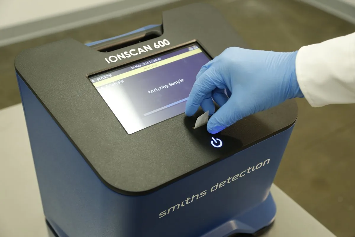 Gloved hand inserting a sample swab while the screen reads Analyzing Sample